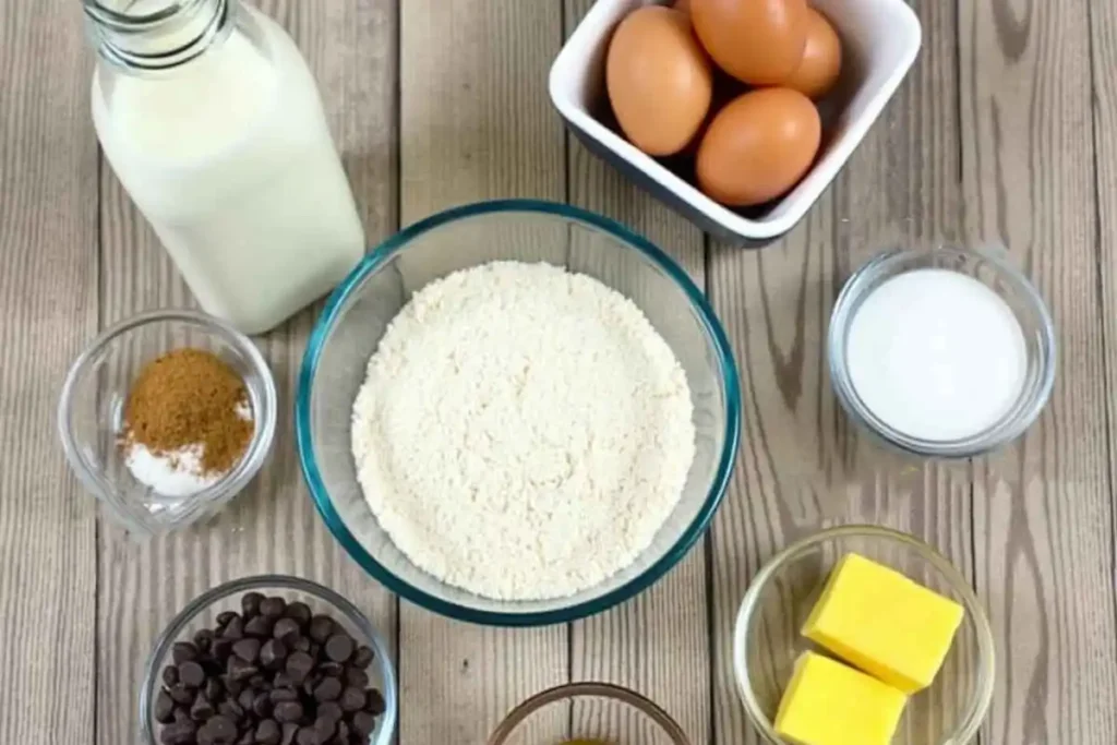 Ingredients for a kefir sheet cake recipe, including kefir, eggs, flour, sugar, butter, milk, and chocolate chips, neatly arranged on a wooden surface.